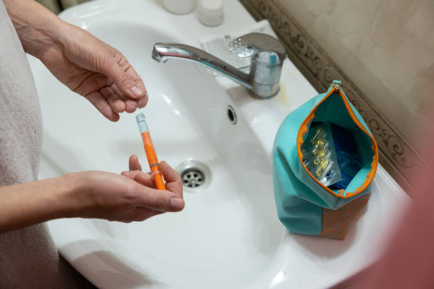 The woman takes an estrogen gel from the syringe. She stands in front of the bathroom sink wrapped in a towel after taking a shower.